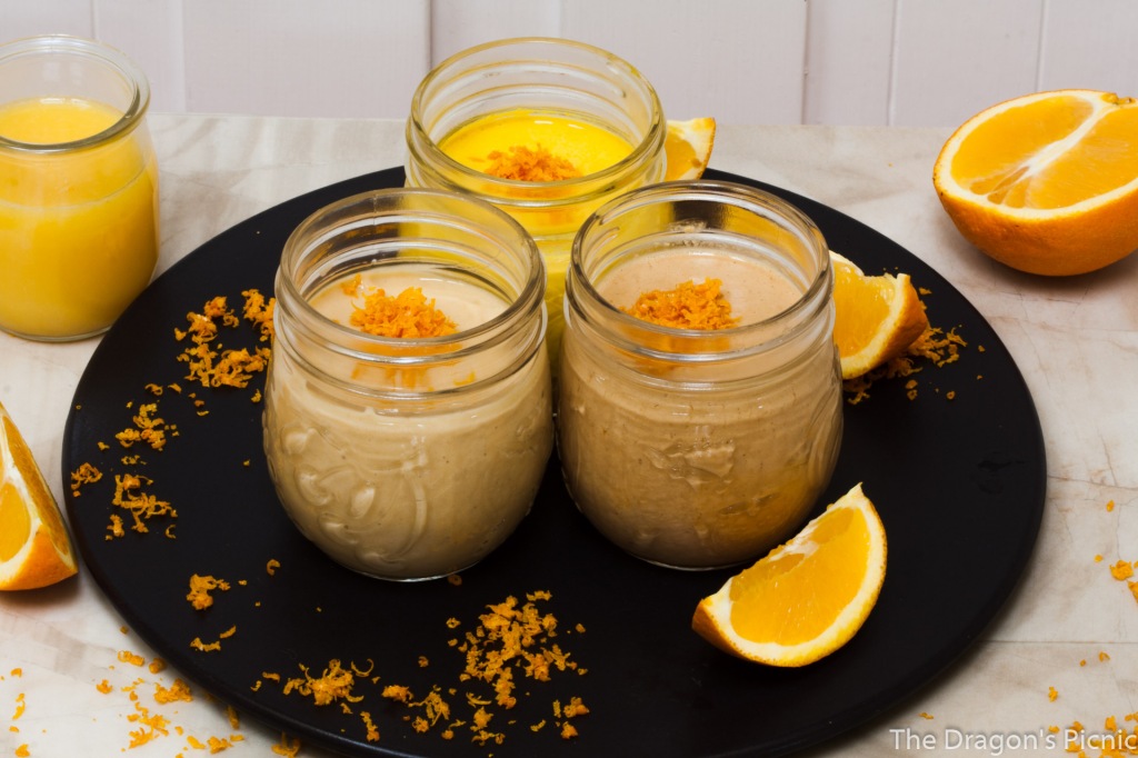 3 jars of orange tahini based sauces with orange segments in foreground and oranges in background