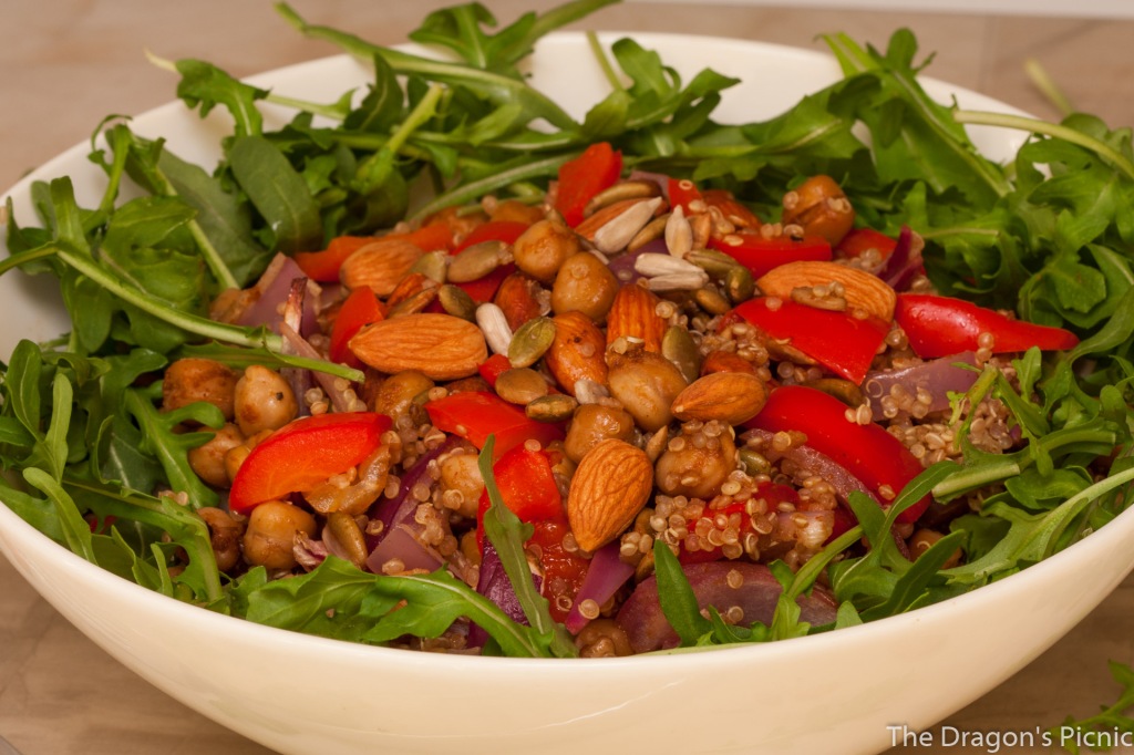 close up of white bowl with spiced almond and quinoa salad on bed of arugula